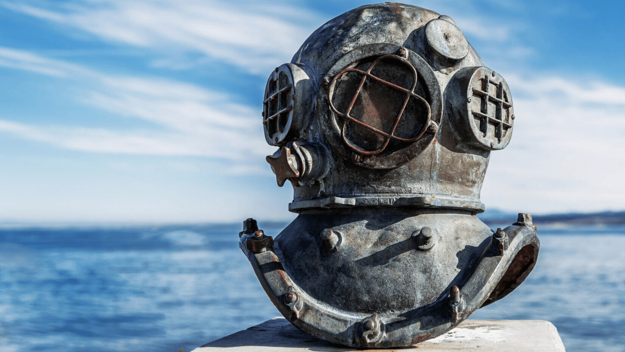 sept-blog-history-of-scuba-diving.png Old scuba diving helmet with ocean background.