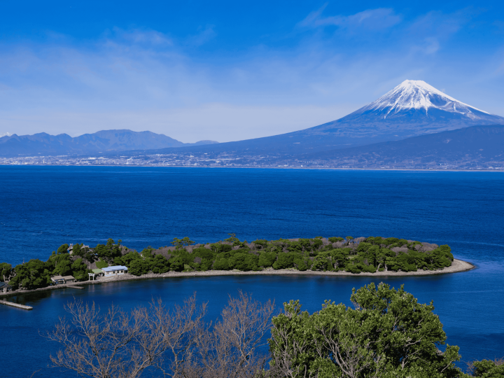 Panoramic view of Mount Fuji seen from Osezaki Cape, with clear blue sea and rocky shoreline